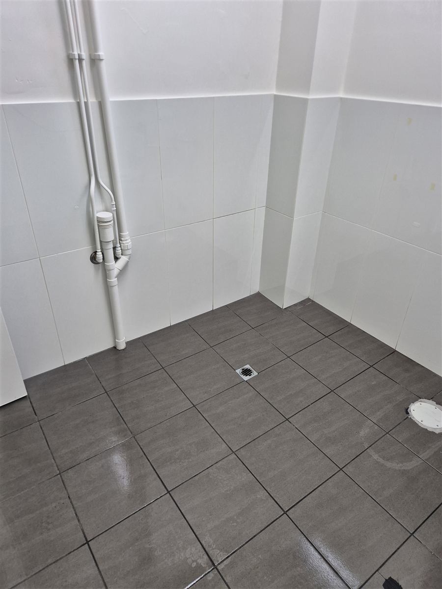 A closer view of the same tiled floor after cleaning, showing the drain and tiles beside the wall pipes