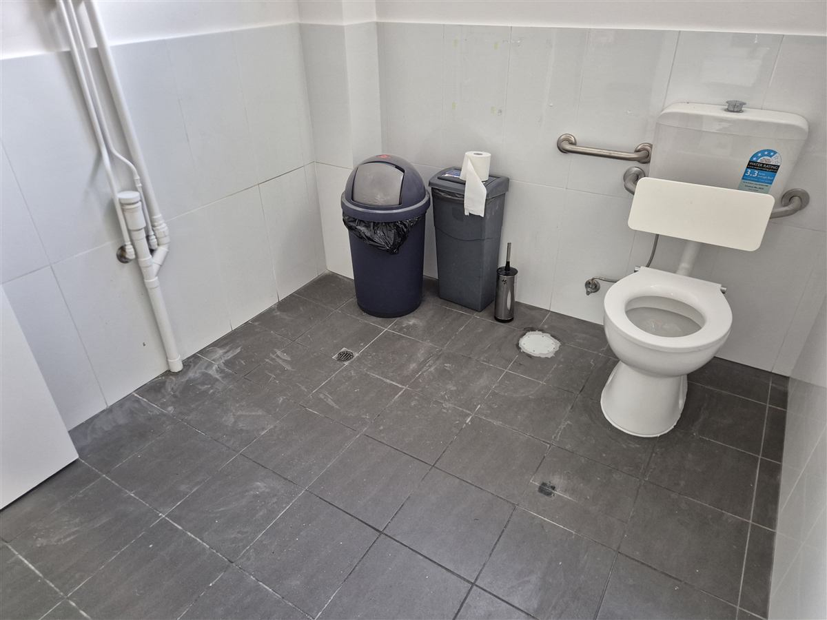 Dust and footprints on grey tiles in an accessible toilet before floor cleaning