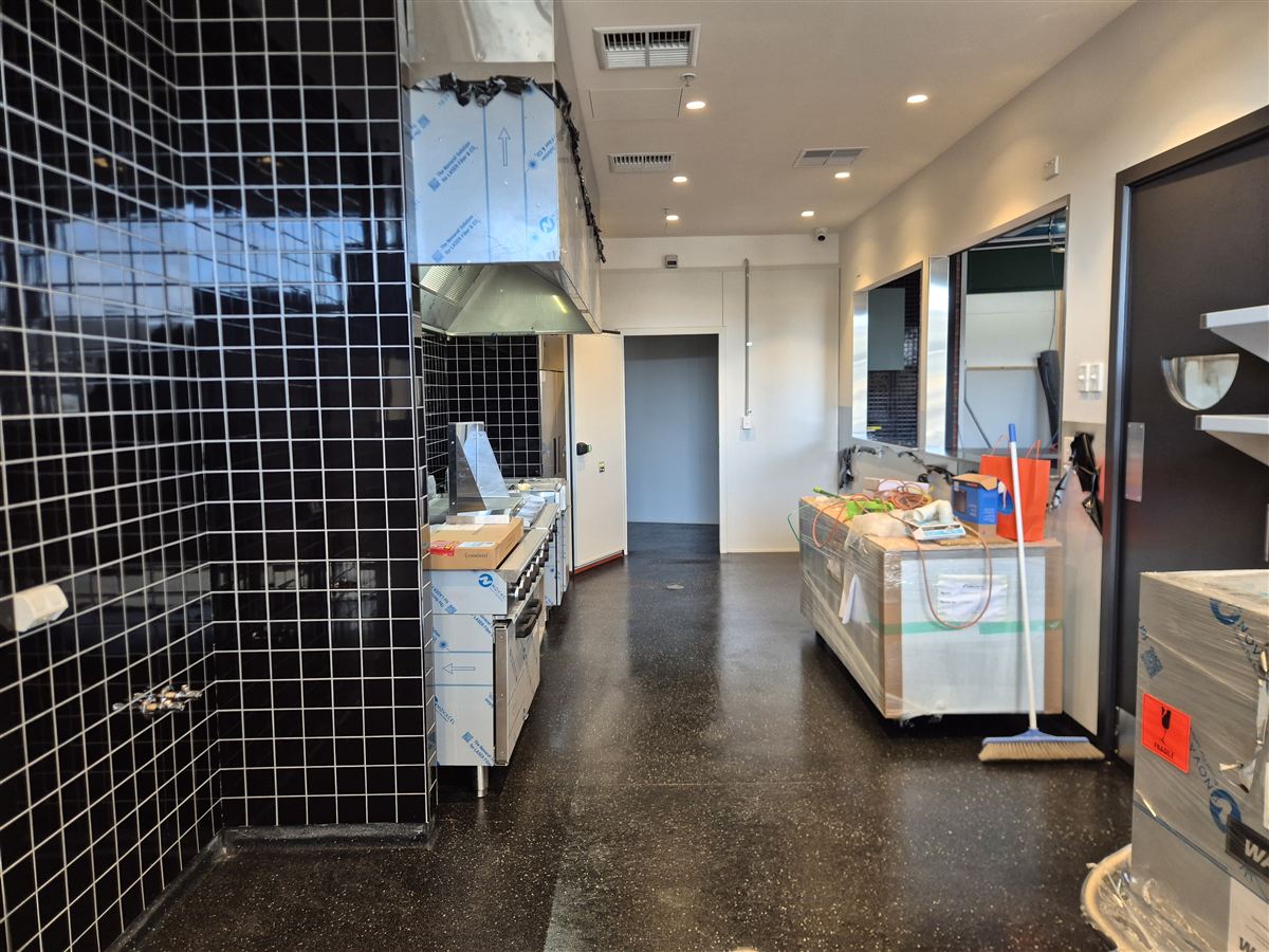 The same café kitchen with a cleared and cleaned floor; appliances remain wrapped while fit-out work continues
