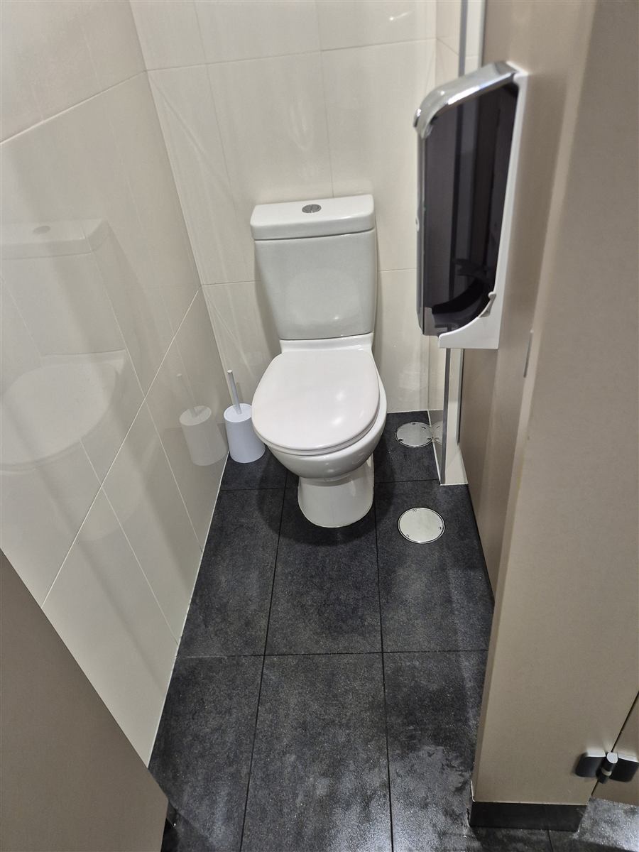 The same toilet cubicle after cleaning, with clear floor tiles and two circular floor covers on the right