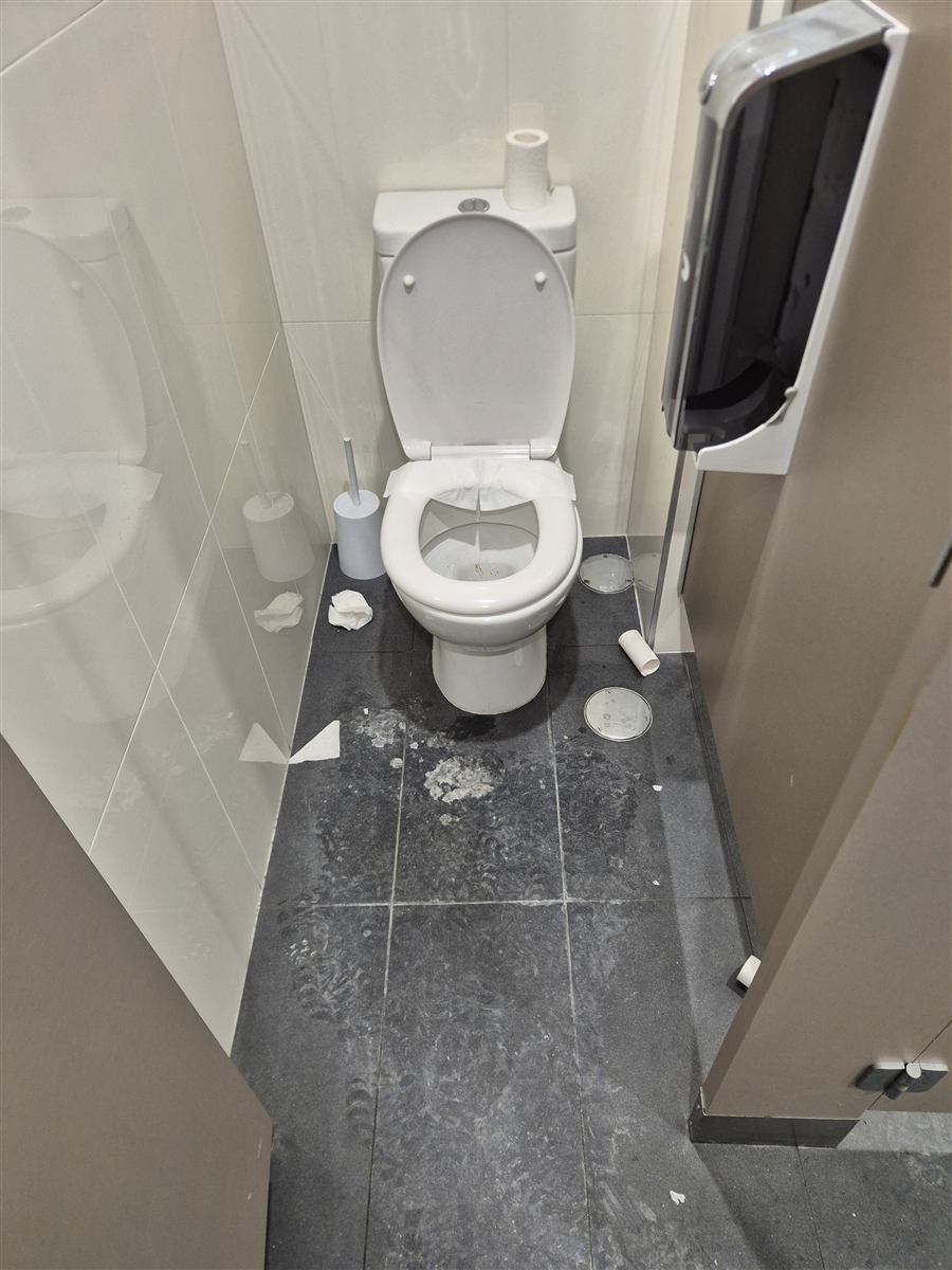 Paper debris and residue on dark floor tiles in a toilet cubicle before cleaning